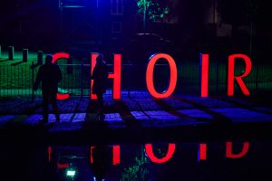 Two people walk down a canal towpath at night as 1.5 metre high letters spell out the word CHOIR